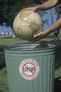 Hands holding a globe over a park trash receptacle