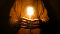 Hands holding glowing light bulb in front of torso on dark background. A pair of hands are gently holding a brightly Royalty Free Stock Photo