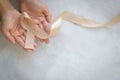 Hands holding gold ribbon on white fabric background with copy space. The international awareness symbol for Childhood Cancer. Royalty Free Stock Photo