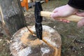 Hands holding a hammer hammer an iron wedge into a log.