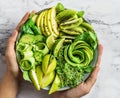 Hands holding healthy fresh green salad with avocado, kiwi, apple, cucumber, pear, greens and sesame on light marble background. Royalty Free Stock Photo