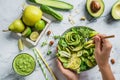 Hands holding healthy fresh summer salad with avocado, kiwi, apple, cucumber, pear, greens and sesame with smoothie on light Royalty Free Stock Photo