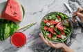 Hands holding healthy fresh summer watermelon salad with arugula, spinach, feta cheese and greens on light marble background. Royalty Free Stock Photo