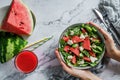 Hands holding healthy fresh summer watermelon salad with arugula, spinach and greens on light marble background. Healthy food, Royalty Free Stock Photo