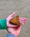 Hands Holding Heart Shaped Rock against neutral background.