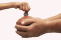 Hands Holding Indian penny bank made with mud clay and Child hand adding coin into the earthen pot or terracotta piggy bank on