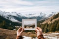 Hands holding an instant photo of a mountain landscape