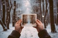 Hands holding an instant photo of a winter forest