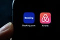 Hands holding iPhone 11 with Airbnb and booking.com service icons.