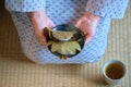 Hands holding japanese Kashiwa mochi and green tea on tatami.