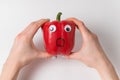 Hands holding large red pepper with funny scared face. Pepper with Googly eyes on white background