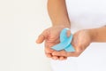 Hands holding light blue color ribbon on white background with copy space. Lymphedema and Prostate Cancer Awareness month symbol. Royalty Free Stock Photo