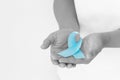 Hands holding light blue color ribbon on white background with copy space. Lymphedema and Prostate Cancer Awareness month symbol. Royalty Free Stock Photo