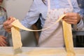 Hands holding long dough thin stripe for pasta cooking