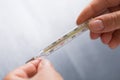Hands holding mercury thermometer which shows febrile temperature on gray background Royalty Free Stock Photo