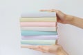 Hands holding a neatly arranged stack of books in soft pastel hues,