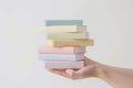 Hands holding a neatly arranged stack of books in soft pastel hues,