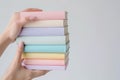 Hands holding a neatly arranged stack of books in soft pastel hues,