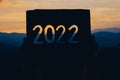 Hands holding of new year 2022 silhouette design from cardboard against the background of mountain with sunset. Happy New Year Royalty Free Stock Photo