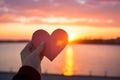 Hands holding a paper-cut heart shape against a sunset Royalty Free Stock Photo