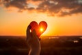 Hands holding a paper-cut heart shape against a sunset Royalty Free Stock Photo
