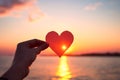 Hands holding a paper-cut heart shape against a sunset Royalty Free Stock Photo