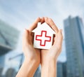 Hands holding paper house with red cross