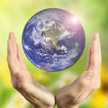 Hands holding the planet on blurred green bokeh background color of a natural tree with leaves, facing the sun-flared