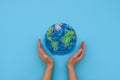 Hands holding planet Earth made from plastic disposable packages on blue background. Save the world, creative, environment