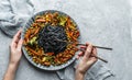 Hands holding a plate of black spaghetti or pasta from seafood with grilled vegetables, broccoli, corn, green peas over light Royalty Free Stock Photo