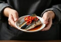 Hands holding plate of grilled mackerel with sliced red chilies and sauce Royalty Free Stock Photo