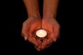 Hands holding and protecting lit or burning candle candlelight on darkness.