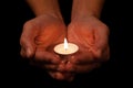 Hands holding and protecting lit or burning candle candlelight on darkness.