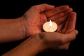 Hands holding and protecting lit or burning candle candlelight on darkness.