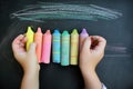 hands holding a range of colorful chalks against a blackboard