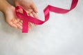 Hands holding Red burgundy ribbon bow on white fabric background with copy space, symbol of Multiple Myeloma or Plasma cell cancer Royalty Free Stock Photo