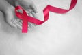 Hands holding Red burgundy ribbon bow on white fabric background with copy space, symbol of Multiple Myeloma or Plasma cell cancer Royalty Free Stock Photo