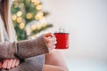 Hands holding a red cup of hot chocolate with marshmallows on Christmas tree lights bokeh background Royalty Free Stock Photo