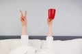 Hands holding red cup and V sign stick out under the blanket Royalty Free Stock Photo