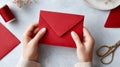 Hands holding red envelope over craft workspace surface Royalty Free Stock Photo
