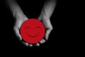 Hands holding red happy smile on black background.