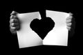 Hands holding +and ripping sheet of paper with torn heart shape against black background Royalty Free Stock Photo