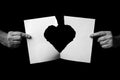 Hands holding +and ripping sheet of paper with torn heart shape against black background Royalty Free Stock Photo