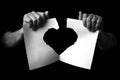 Hands holding +and ripping sheet of paper with torn heart shape against black background Royalty Free Stock Photo