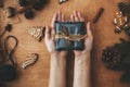 Hands holding  rustic christmas gift in black wrapping paper with cinnamon decoration, and pine branches, cones, gingerbread Royalty Free Stock Photo