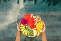 Hands holding served fruit plate above hotel pool. Exotic summer diet.