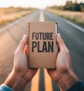Hands holding a small brown spiral notebook with the words Future Plan on a road at sunset Royalty Free Stock Photo