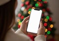 Hands holding smartphone with blank screen against blurred Christmas tree lights and bokeh Royalty Free Stock Photo