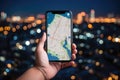 Hands holding a smartphone with a navigation map on the screen on a blurred background of a city with skyscrapers, night time Royalty Free Stock Photo