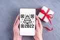 Hands holding a smartphone, tablet, mobile phone with a qr code screen in the shape of a Christmas tree date 2022 Royalty Free Stock Photo